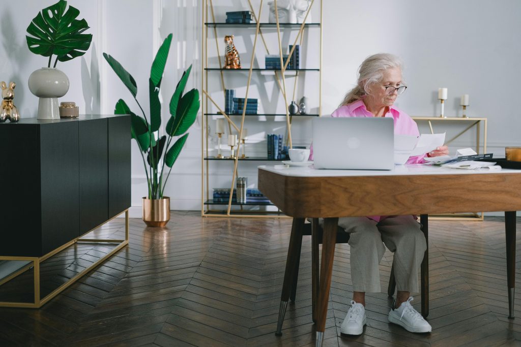 ältere Frau sitzend vorm Laptop und Dokument lesend